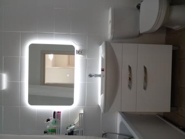 Установлено зеркало с подсветкой, закреплён умывальник с тумбой, подключён смеситель, отрегулирована сантехника, обновлены полки для хранения.