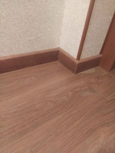 Установлен плинтус, аккуратно скрывающий стык между стеной и полом. Завершена работа по монтажу, обеспечив плавный переход и эстетичный вид. Все элементы надежно закреплены.