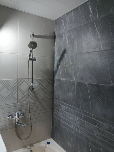 На стенах ванной комнаты аккуратно уложена керамическая плитка с геометрическим узором, создающая стильный и современный интерьер. Швы ровные, поверхность гладкая.