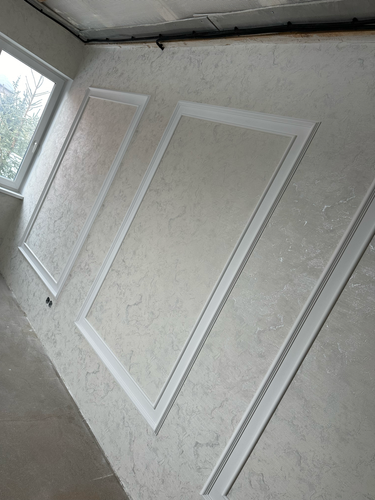 На стене аккуратно размещены декоративные панели с текстурой, обрамленные белыми молдингами, создающими элегантный и стильный вид. Завершенная работа придает комнате изысканность.