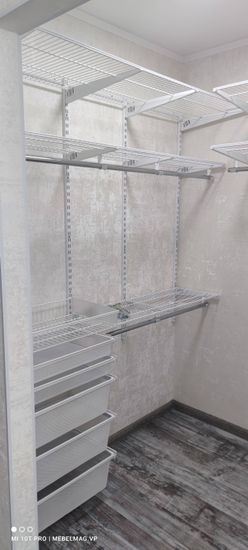 Установлены металлические стеллажи с сетчатыми полками и выдвижными корзинами. Конструкция закреплена на стене, обеспечивая устойчивость и функциональность для хранения вещей.