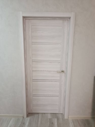 Установлена светлая деревянная дверь с металлической ручкой. Полотно ровно закреплено в проеме, наличники аккуратно подогнаны, обеспечена плавная работа механизма.