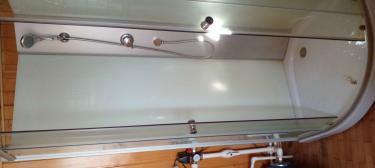 На изображении представлена душевая кабина, установленная в помещении. Видны стеклянные двери, металлические элементы и подключенные трубы. Всё выглядит аккуратно и функционально.