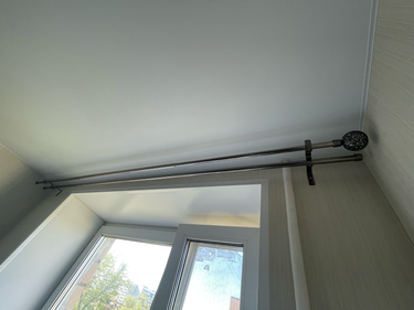 Установлен новый карниз для штор над окном, закрепленный на стене. Металлическая конструкция надежно зафиксирована, готова к использованию.