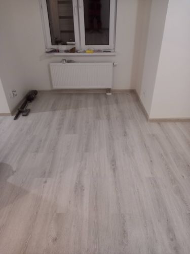 Обновлённое покрытие уложено в комнате, панели ровно подогнаны, плинтусы установлены, стыки аккуратные, поверхность гладкая, цвет светлый, создаёт уютную атмосферу.