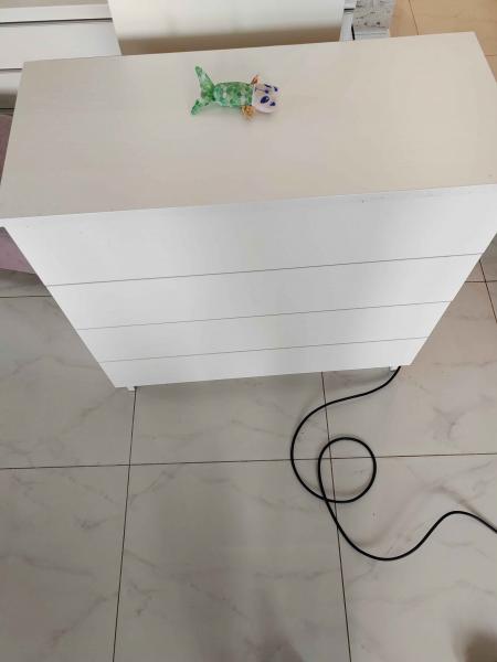 Собран белый комод с четырьмя ящиками, установлен на плиточный пол. Все элементы надежно закреплены, конструкция устойчива и готова к использованию.