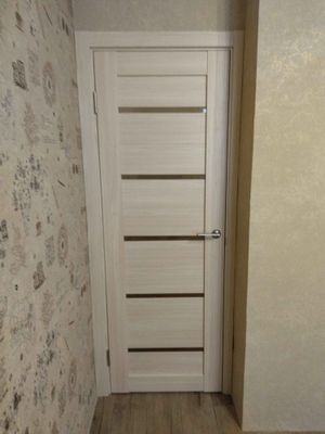 Установлена новая дверь, уменьшен проем, выровнены стены, добавлены наличники, обновлено покрытие пола, поклеены обои. Завершено оформление, обеспечена функциональность и эстетика.