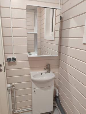 Изображение демонстрирует завершённый монтаж сантехники: установлены раковина с тумбой, смеситель, подключены трубы для воды и канализации, закреплён шкафчик с зеркалом.